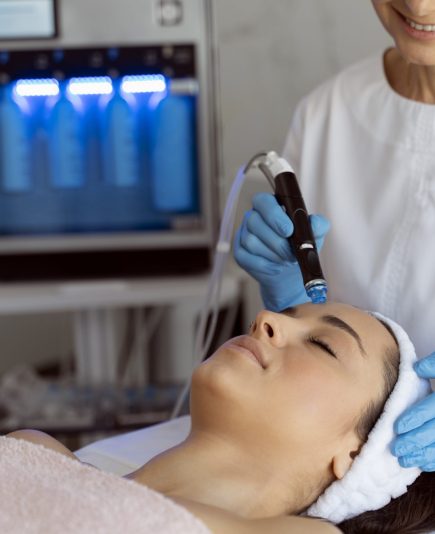 Professional female cosmetologist doing hydra-facial procedure in cosmetology clinic. Doctor using hydra vacuum cleaner. Rejuvenation and cosmetology concept