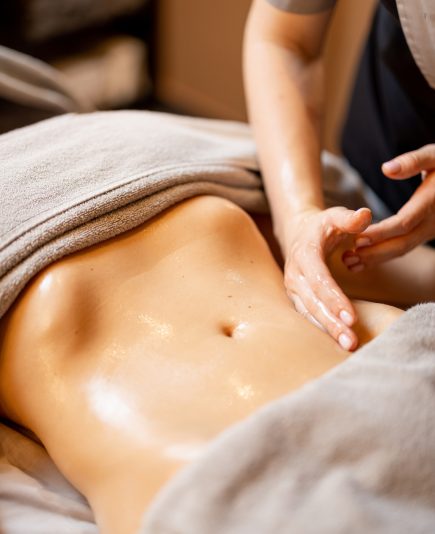 Masseuse performs professional abdominal massage for female client lying on a couch, close-up on hands