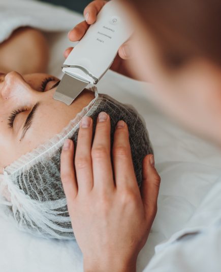 Top view of a woman receiving ultrasound cavitation facial peeling in spa salon. Happy face. Cosmetology beauty procedure. Facial skincare.