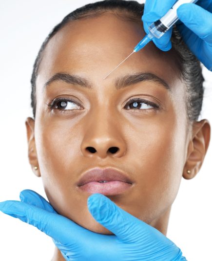 Studio closeup of an attractive young woman receiving a botox injection in her face while standing against a white background