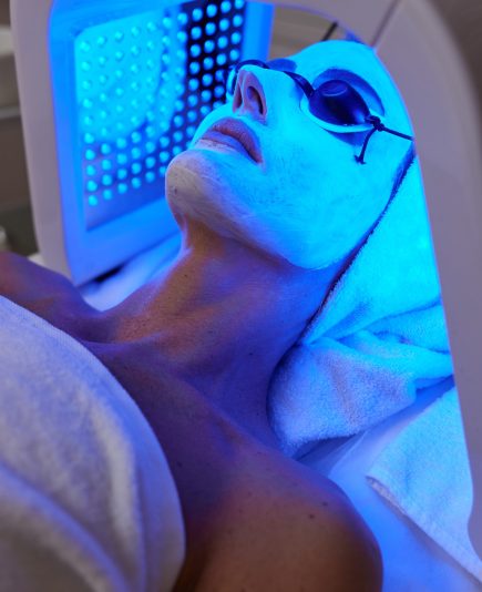 Woman in protective glasses getting facial treatment with led therapy. LED mask at the beauty clinic