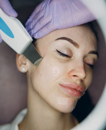 Woman receiving cleansing therapy with a professional ultrasonic equipment in cosmetology beauty spa.